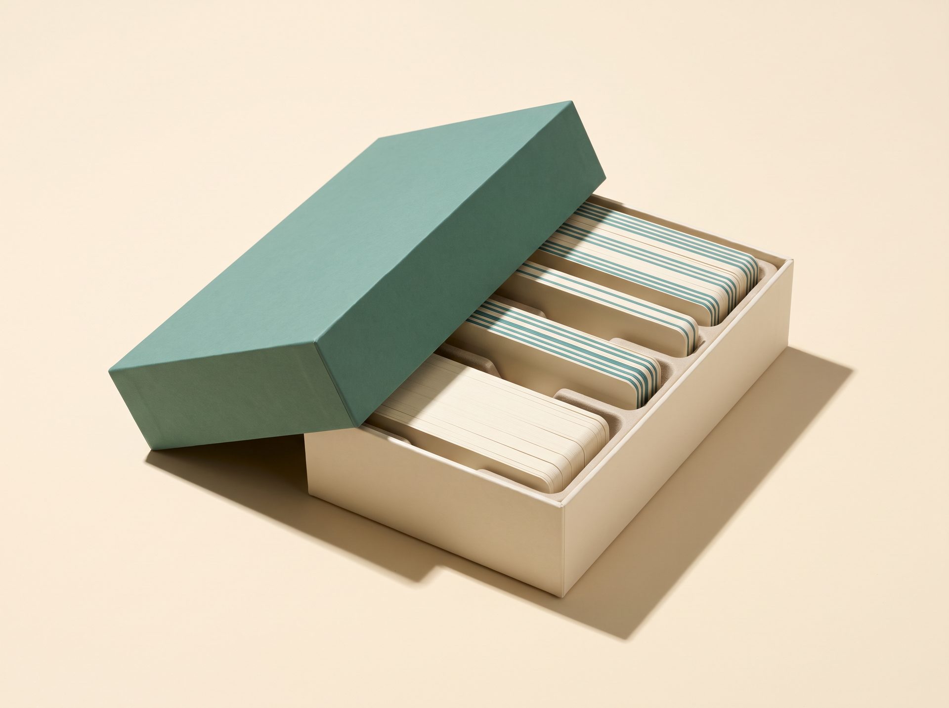 A cream box with a teal lid resting open at an angle, divided compartments inside holding stacks of cards.