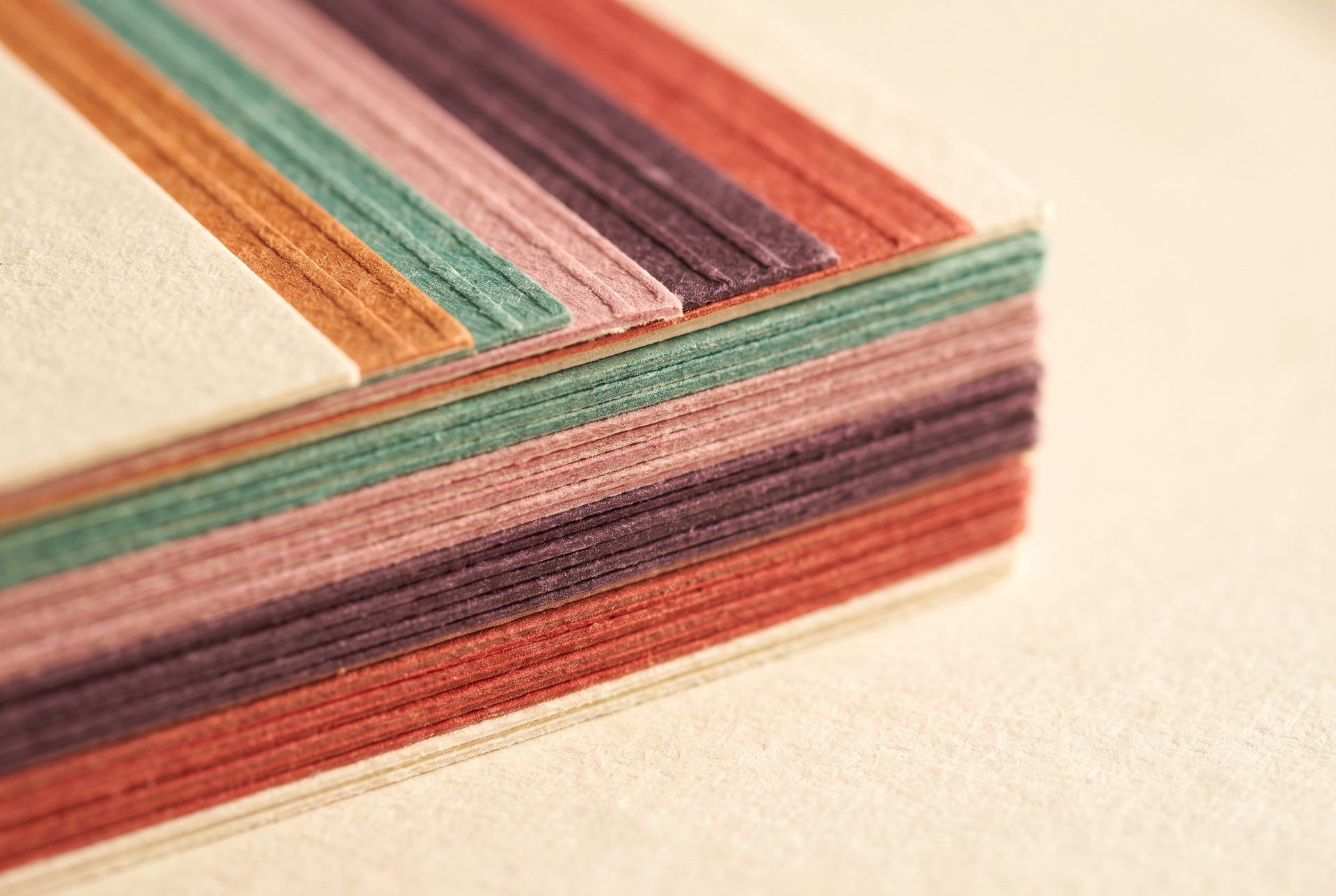Close-up of a stack of cards, their painted edges showing five colours: copper, teal, pink, plum and red